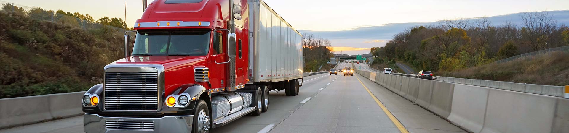 Red semi-truck tractor trailer 18 wheeler on highway at sunrise.