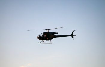 A black helicopter is flying in the clear blue sky.